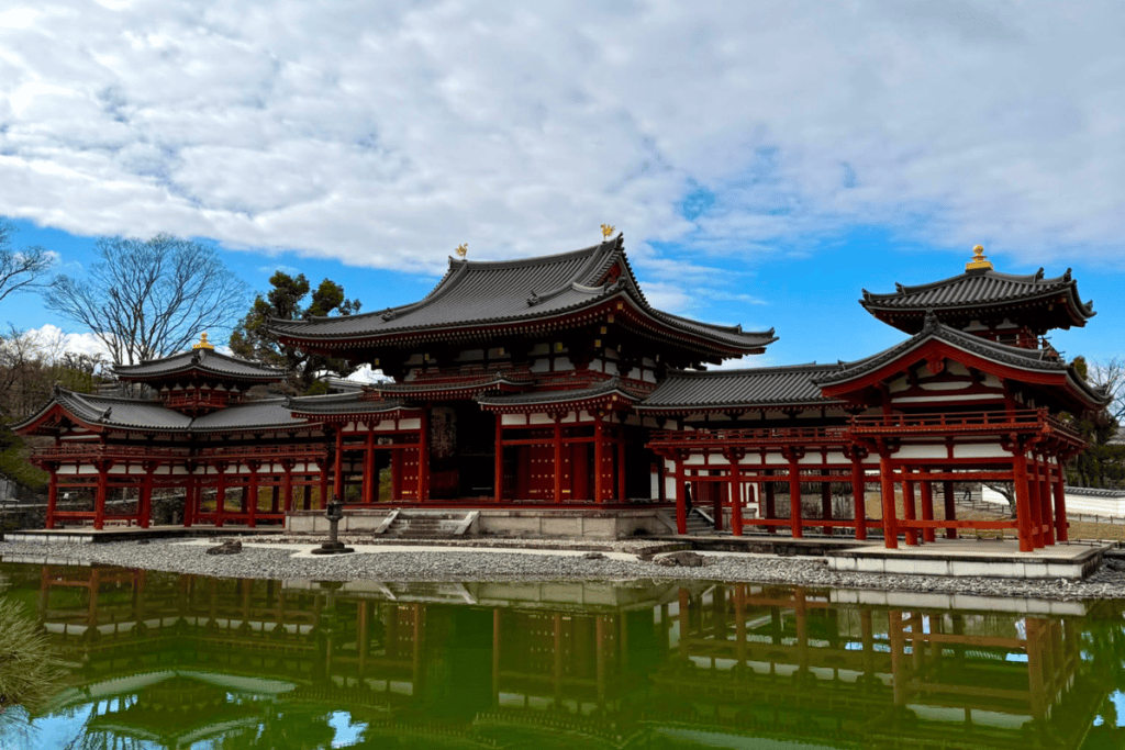 Die historische rot-braune Phönix-Halle des Byōdō-in Tempels in Uji, die sich spiegelglatt auf der Wasseroberfläche des davorliegenden Teichs spiegelt.