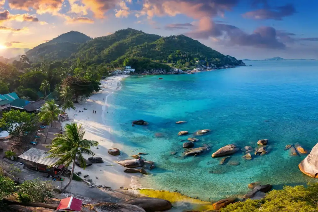 Bucht mit Sandstrand und bewaldeten Felsen in Thailand bei Sonnenuntergang
