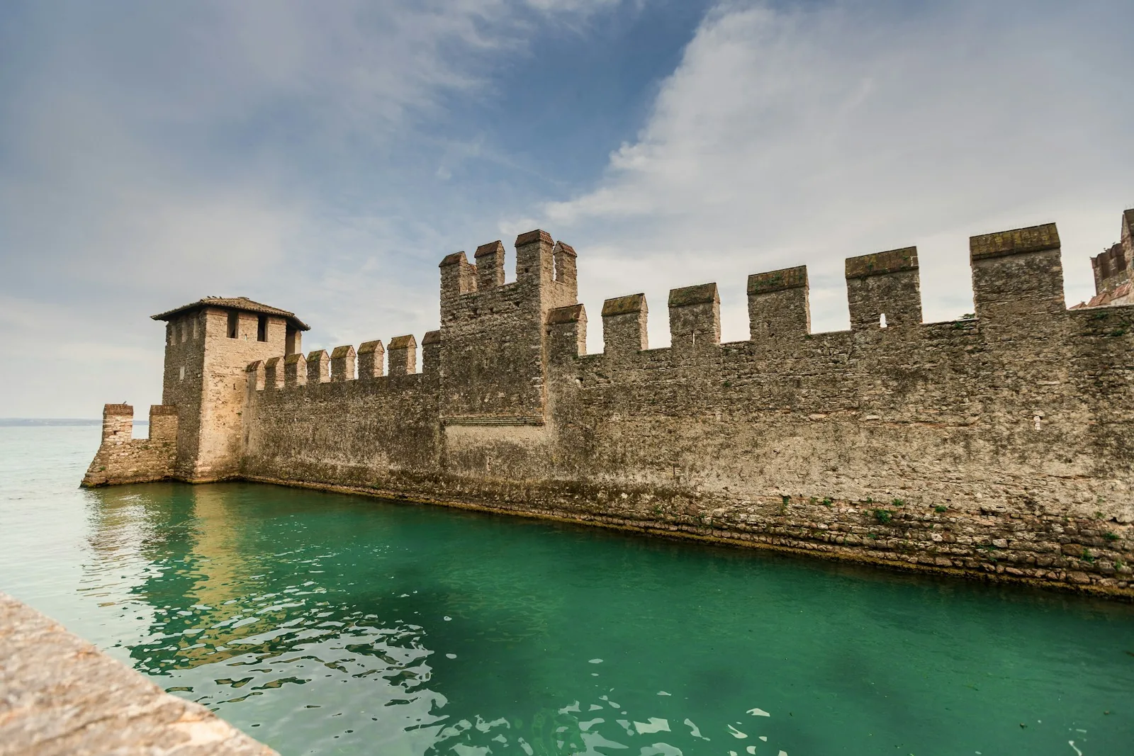 Zinnenmauer der Scaligerburg von Sirmione über dem türkisen Wasser des Gardasees