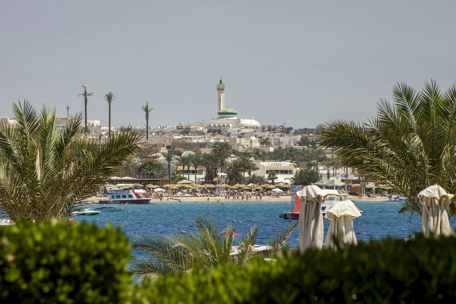 Palmen und Sonnenschirme am Strand von Hurghada, dahinter eine Moschee mit hohem Minarett