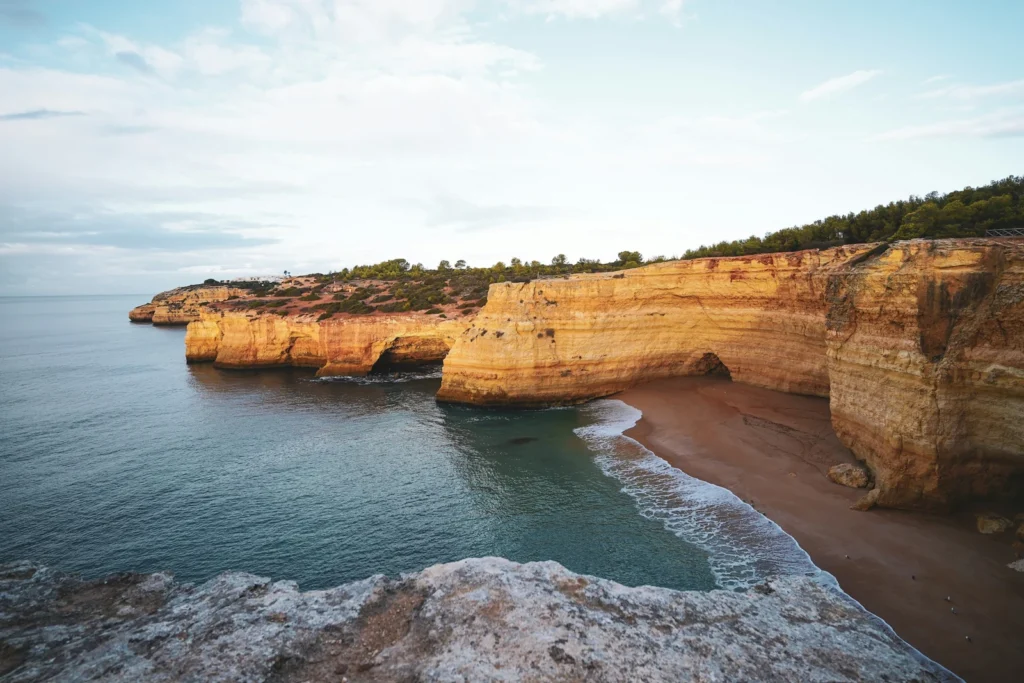 Goldgelbe Felsklippen mit kleinem Sandstrand und ruhigem Meer an der Algarve