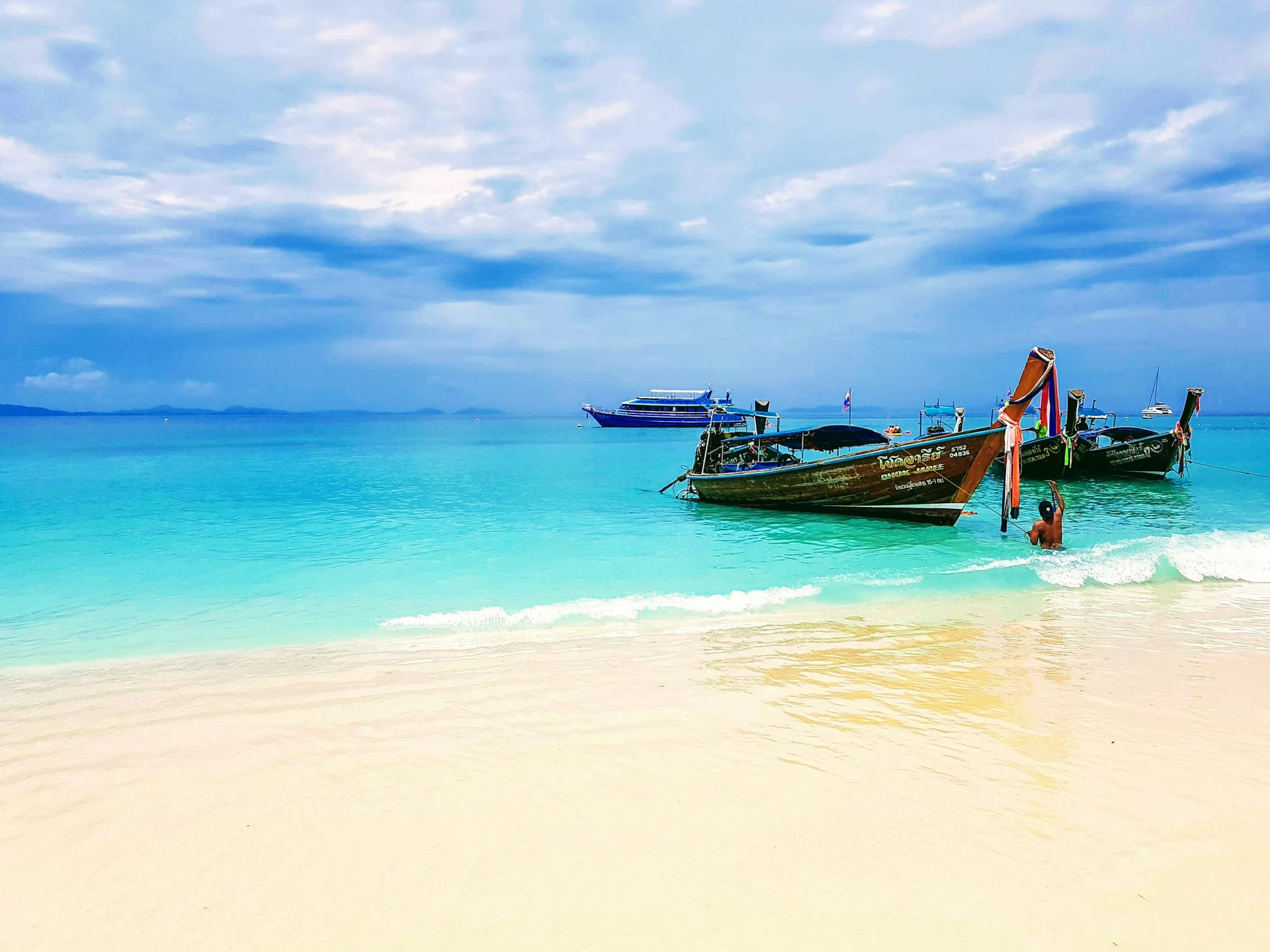 Longtailboote im türkisen Wasser an einem weißen Sandstrand in Thailand