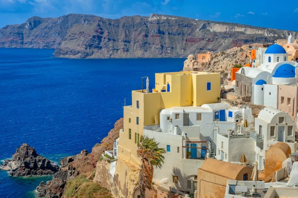 Weiße und gelbe Häuser mit blauen Kirchenkuppeln an der Steilküste von Oia über der Caldera von Santorini